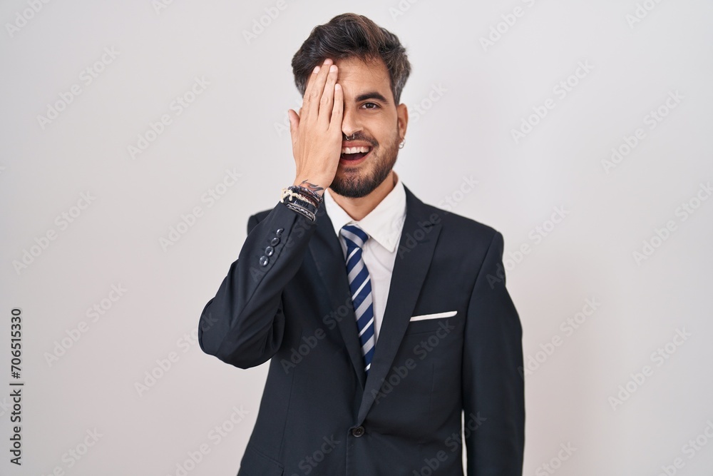Young hispanic man with tattoos wearing business suit and tie covering one eye with hand, confident smile on face and surprise emotion. Young hispanic man with tattoos wearing business suit and tie covering one eye with hand, confident smile on face and surprise emotion.