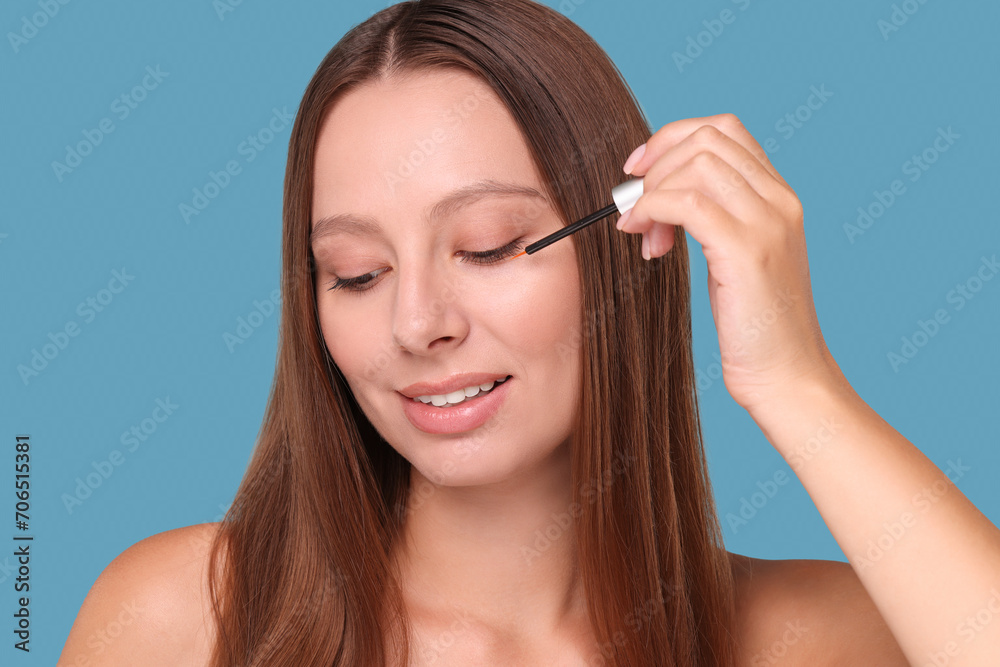 Beautiful woman applying serum onto eyelashes on light blue background Beautiful woman applying serum onto eyelashes on light blue background