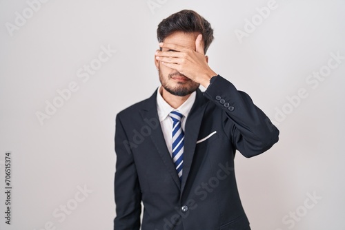 Young hispanic man with tattoos wearing business suit and tie covering eyes with hand, looking serious and sad. sightless, hiding and rejection concept © Krakenimages.com