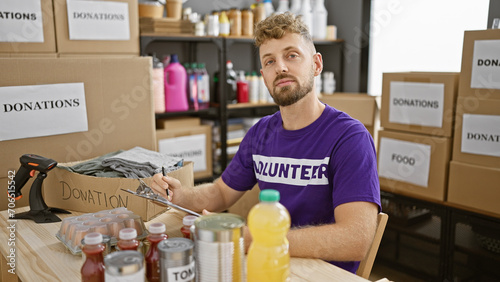 Handsome young man with a beard volunteering in a donation center, surrounded by boxes of food and other items.