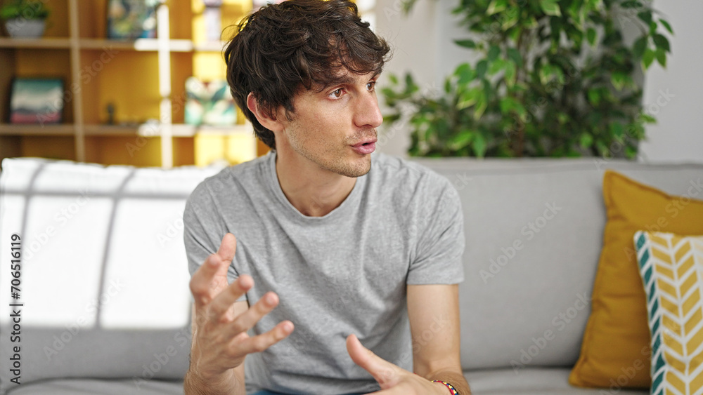 Fototapeta premium Young hispanic man looking to the side sitting on sofa speaking at home