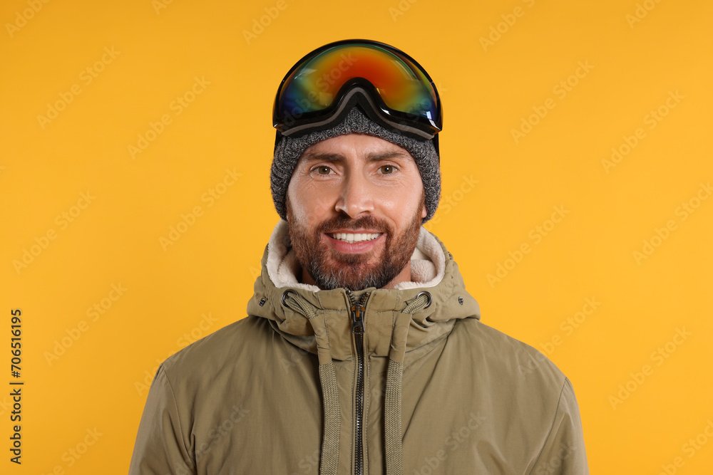 Fototapeta premium Winter sports. Happy man in ski suit and goggles on orange background