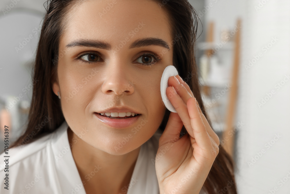Young woman cleaning her face with cotton pad in bathroom, closeup Young woman cleaning her face with cotton pad in bathroom, closeup