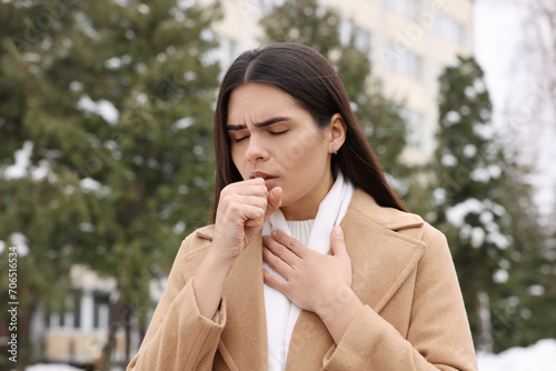 Woman in coat coughing outdoors. Cold symptoms