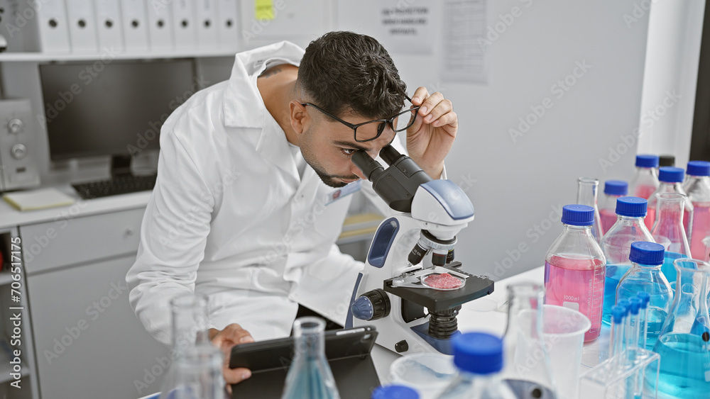 A focused man using a microscope in a laboratory setting, surrounded by scientific equipment and samples. A focused man using a microscope in a laboratory setting, surrounded by scientific equipment and samples.