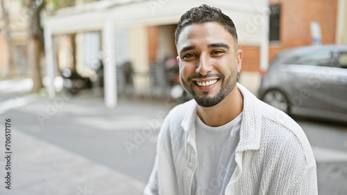 Handsome man smiling on a city street while wearing a white cardigan in a candid urban setting. photo