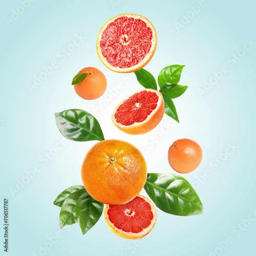 Fresh grapefruits and green leaves falling on light blue background