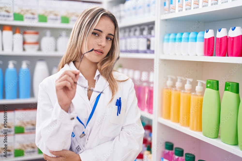 Young blonde woman pharmacist holding glasses at pharmacy