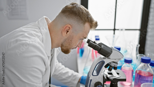 Handsome young man with beard using microscope in laboratory setting, illustrating research and healthcare.