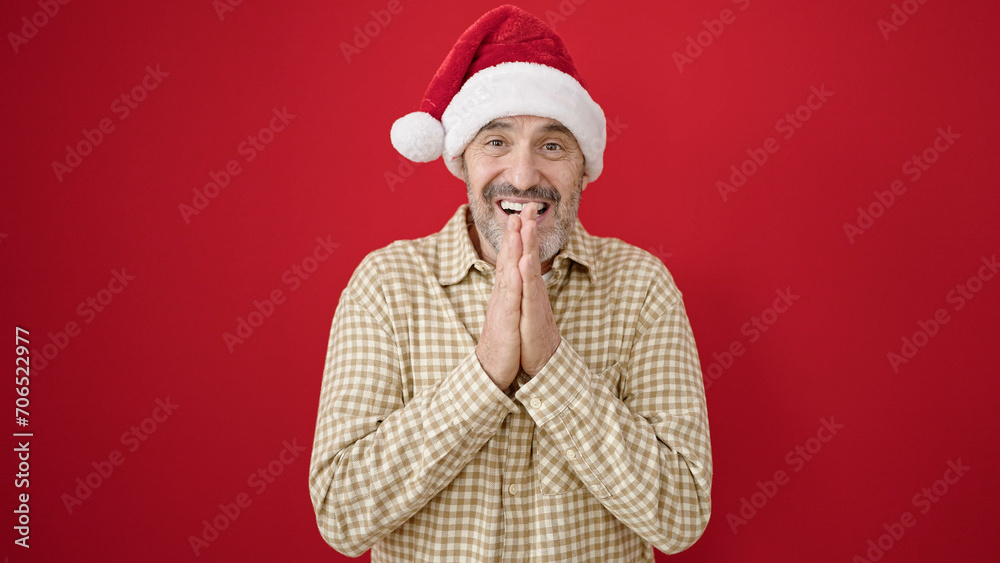 Middle age man smiling confident wearing christmas hat over isolated red background