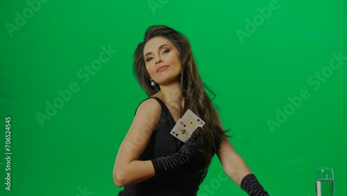 Elegant female in studio on chroma key green screen background. Attractive woman in black dress looking at camera shows ace cards, smiling.