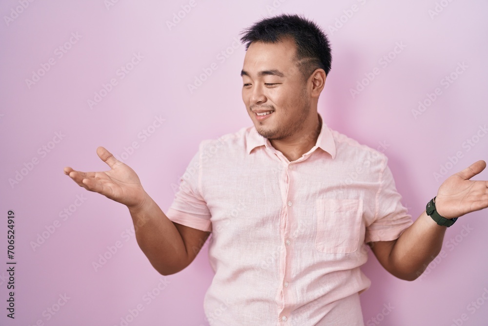 Fototapeta premium Chinese young man standing over pink background smiling showing both hands open palms, presenting and advertising comparison and balance