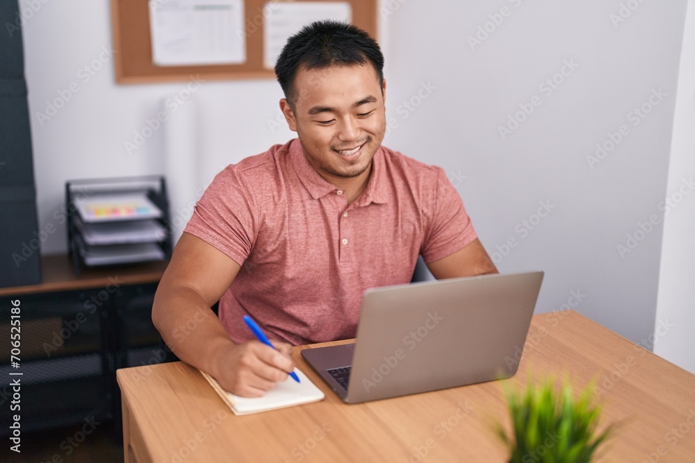 Young chinese man business worker using laptop writing on notebook at office