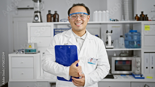 Smiling young chinese scientist  a charming professional man working with confidence and security in the lab  clipboard in hand