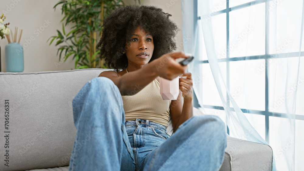 African american woman watching tv sitting on sofa drinking coffee at home African american woman watching tv sitting on sofa drinking coffee at home