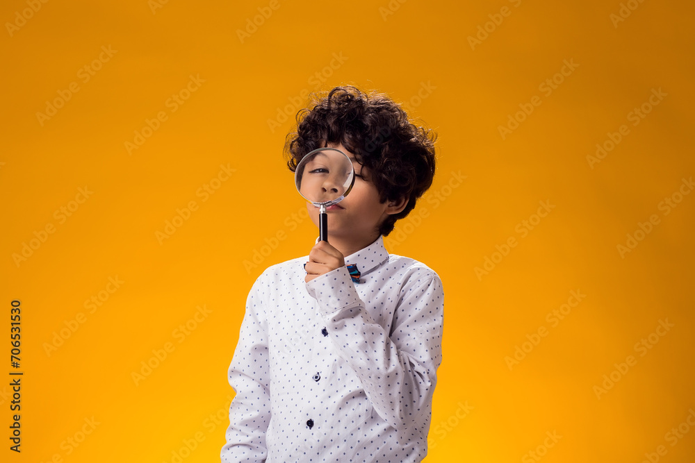 Obraz premium Child boy looking through magnifier over yellow background. Education and curiosity concept