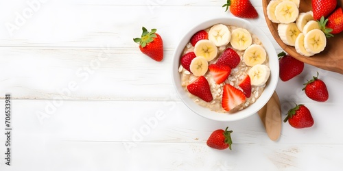 Bowl of oatmeal porridge with strawberry and banana on white table top view. Healthy and diet breakfast.