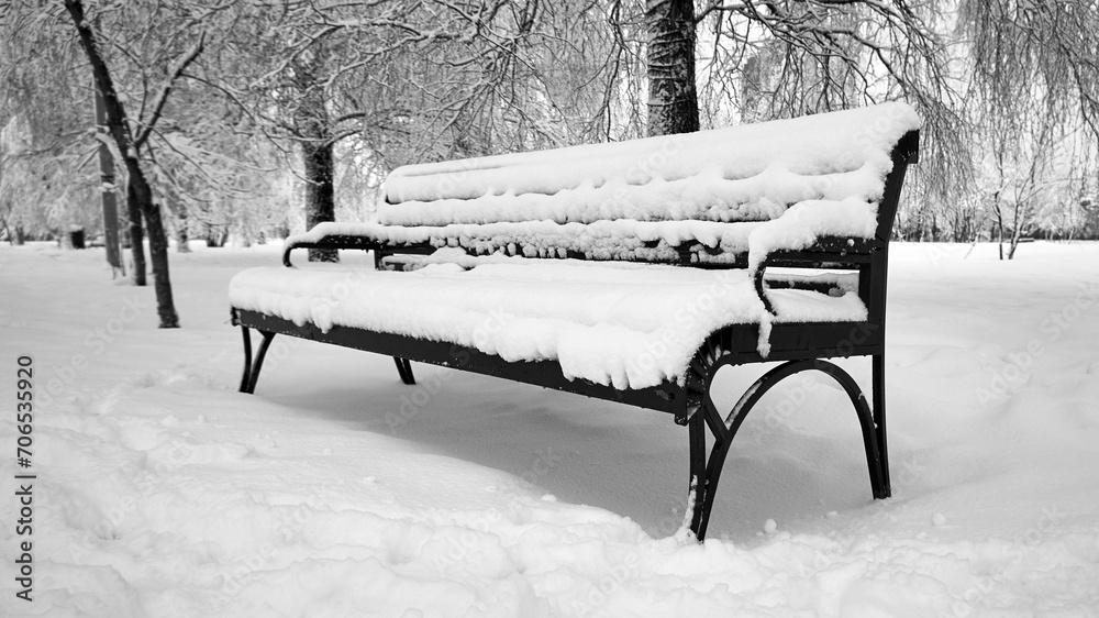 Black and white photo of a park bench covered with snow