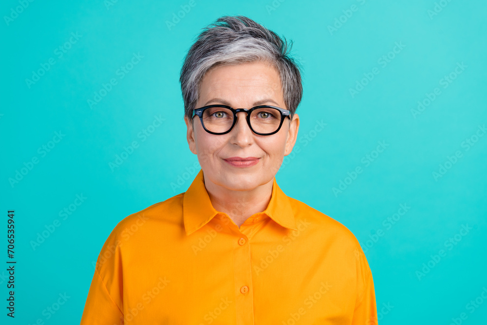 Photo portrait of confident elderly serious woman experienced ceo director wearing orange formal shirt isolated on cyan color background Photo portrait of confident elderly serious woman experienced ceo director wearing orange formal shirt isolated on cyan color background
