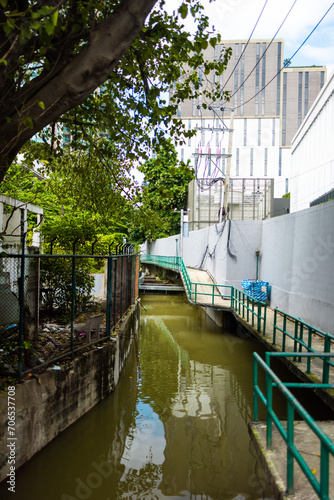 Narrow Canal Flanked by Greenery and Buildings in an Urban Area During Daytime