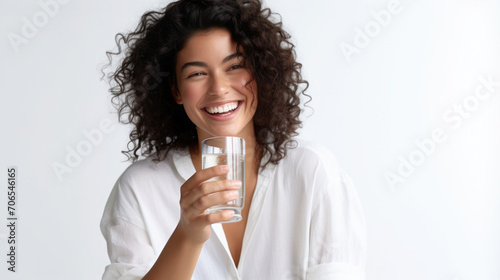 the girl smiles and holds a glass glass of water in her hands, white light background
