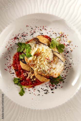 Baked eggplant roll filled with cheese and tomatoes, presented on a pristine white plate, top view