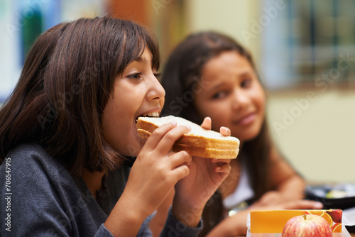Hungry girl  student and eating sandwich in classroom at school for meal  break or snack time. Young kid  person or elementary child biting bread for lunch  fiber or nutrition in class during recess