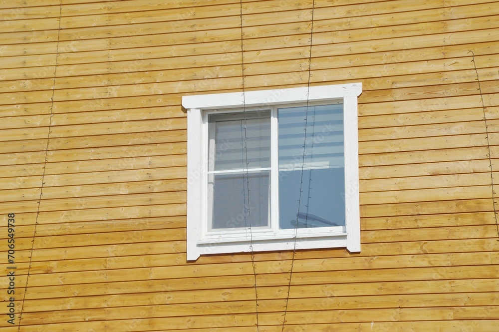 White window on the background of a brown wooden house wall with horizontal boards. Element of a country house.