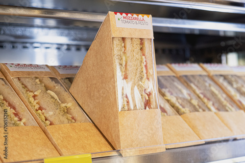 Store display with sandwiches in individual packaging. Sandwiches with mozzarella, tomatoes and pesto in cardboard packaging.