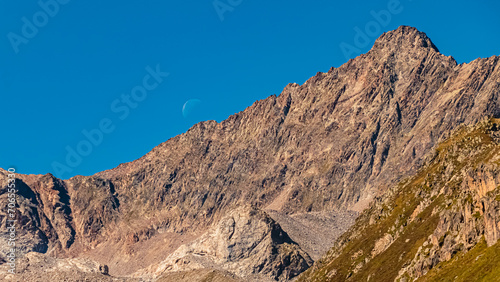Alpine summer view with the moon touching a summit ridge at Lake Rifflsee, Mandarfen, Imst, Tyrol, Austria