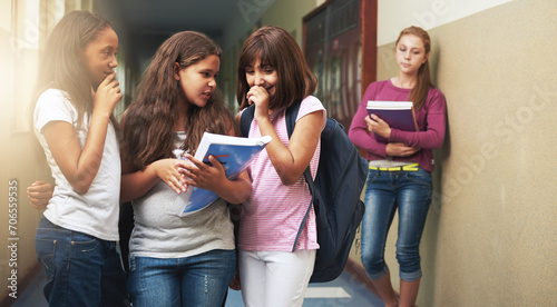 Girls, school and bullying student in gossip, secret or whisper down the corridor or hallway. Group of young kids or children teasing and laughing by lonely learner in verbal abuse outside classroom photo