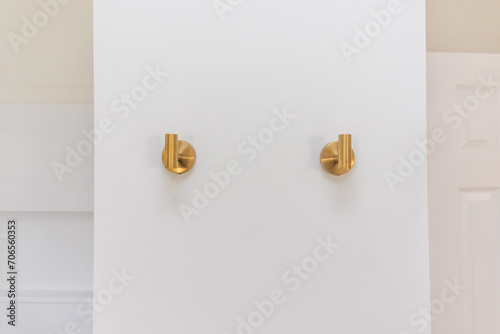 A set of two modern gold towel holder hooks or pegs on an empty blank wall in a bathroom in the interior of a home photo