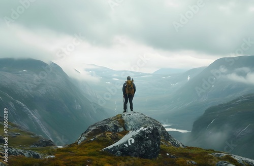 Summit Conqueror - Hiker with Backpack Standing on Top of a Large Rock near Majestic Mountains - solo travel concept © Sri