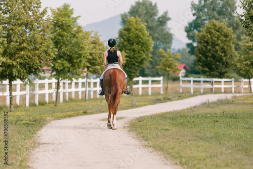 Female rider, horseback riding along the trail that leads between white wood fences and fields. Equestrian leisure activity concept. © 24K-Production