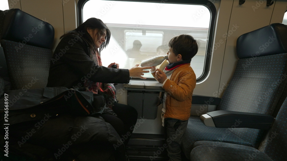 Mother and child traveling by train, little boy eating banana, mom giving son water to drink, family traveling during holidays