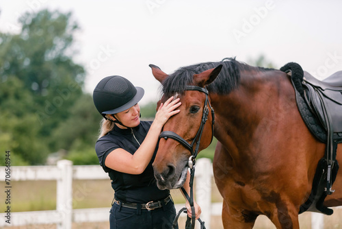Woman with a black helmet stroking a beautiful chestnut horse head, close up shot. Human and animal relation concept.