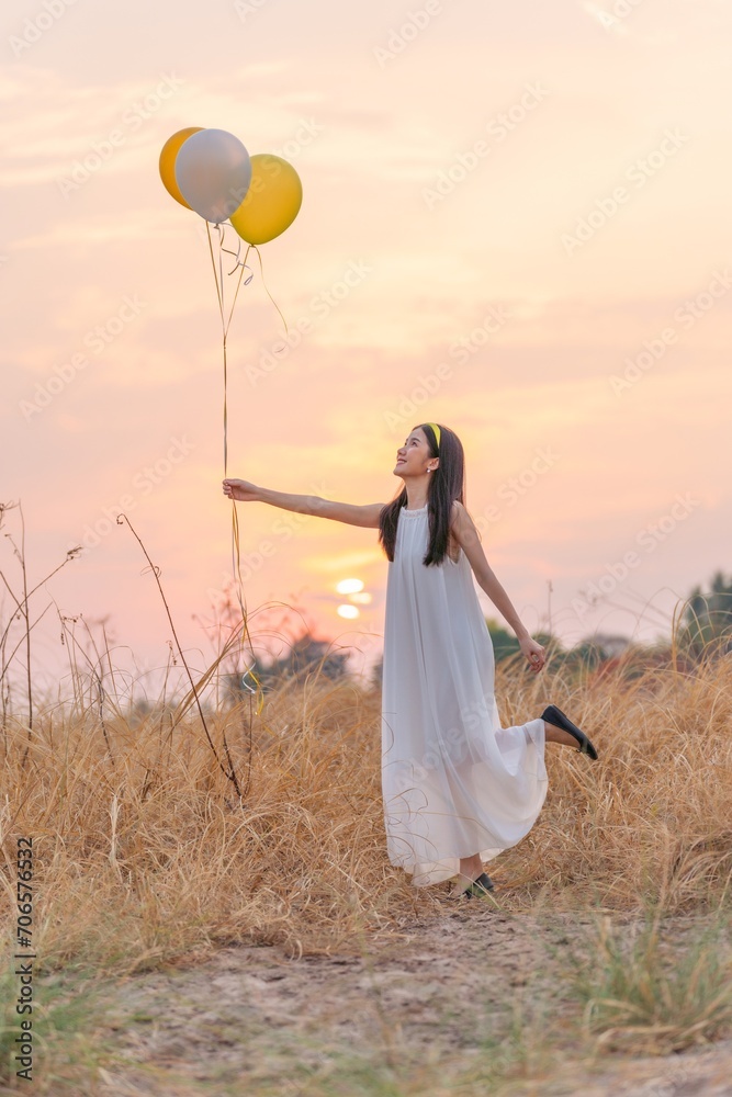 Beautiful girl with balloons in the field. Carefree Serenity: Girl in White Long Dress Embracing Freedom, Holding Balloons in a Dry Grass Meadow