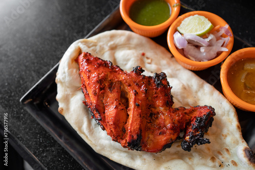 Tandoori chicken with naan in black plates on black table.