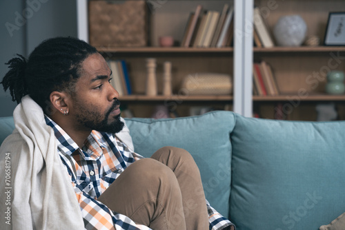 Young depressed African American man sitting on sofa with crossed arms. Racism victim for skin color black male suffering from depression after being fired from work Job lost and mental health concept photo