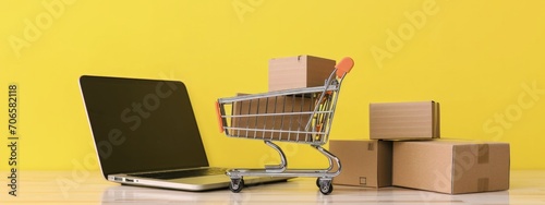 Shopping cart, cardboard boxes and laptop, online shopping concept, technology, yellow background.