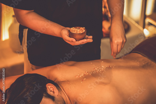 Man customer having exfoliation treatment in luxury spa salon with warmth candle light ambient. Salt scrub beauty treatment in Health spa body scrub. Quiescent photo