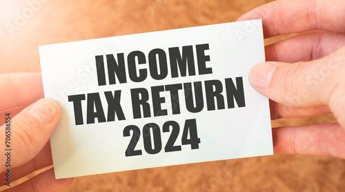 INCOME TAX RETURN 2024 word inscription on white card paper sheet in hands of a businessman.