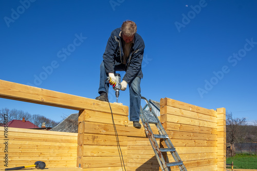 a man builds a wooden house made of profiled timber in the countryside against the blue sky