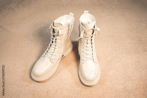 Beige winter women s leather boots on a beige background. Beautiful modern Shoes for bad weather wearing.