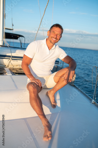 Man in white tshirt sitting on a yacht with a rope in hands