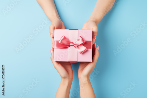 Female hands hold a pink gift box with on the blue background. Background with place for text, copyspace for the holiday, mother's day etc.