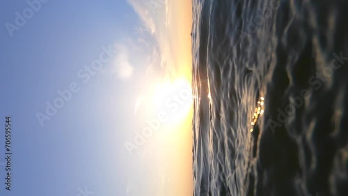 Sea and sun. Sea water surface with ripple waves and sunny path. Shining sun at dawn and sunset. Blue sky with white feather clouds. Open sky sea. Bottom angle. Natural background Vertical