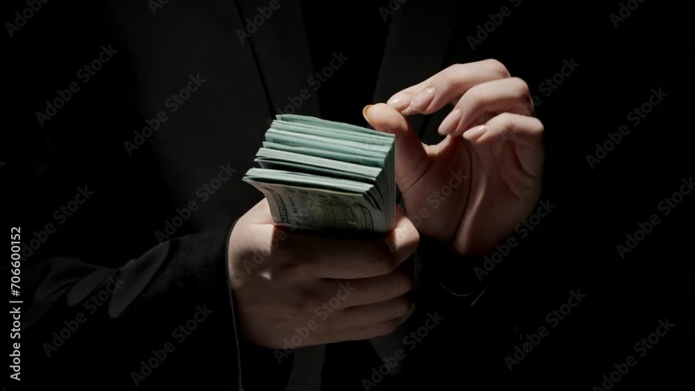 Portrait of female in black suit isolated on black background in low light. Close up shot woman holding flipping tapping wad of dollar banknotes. Portrait of female in black suit isolated on black background in low light. Close up shot woman holding flipping tapping wad of dollar banknotes.