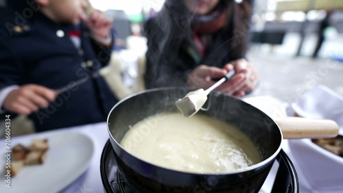 Traditional Swiss food, closeup hand holding fork with bread dipping in cheese, peopel enjoying winter food in cold weather