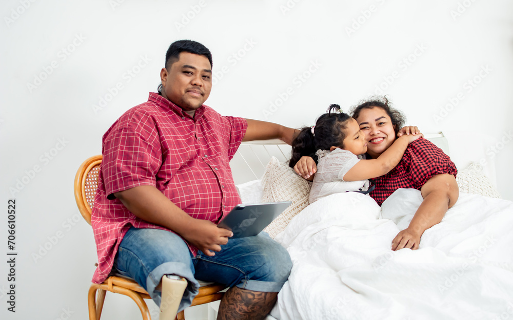 Three people asian family including little daughter, mother and father with handicap prosthetic leg kissing, telling story before bed with warmth, love. Relationship, Family, Education Concept. Three people asian family including little daughter, mother and father with handicap prosthetic leg kissing, telling story before bed with warmth, love. Relationship, Family, Education Concept.